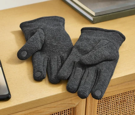 Deux gants en sweat sont posés sur une commode en bois à côté d'un téléphone portable.