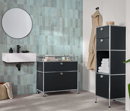 Dans une salle de bain, une commode étroite en métal « CN3 » avec deux tiroirs et 1 compartiment abattant et une commode métallique « CN3 » avec 1 tiroir et 1 compartiment à abattant.