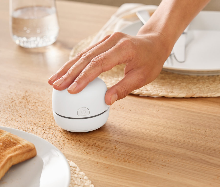 Une main allume un petit appareil blanc sur une table en bois à côté d'un verre d'eau.