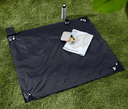 Couverture de pique-nique bleu foncé avec des collations, une thermos et une carte sur une pelouse verte.