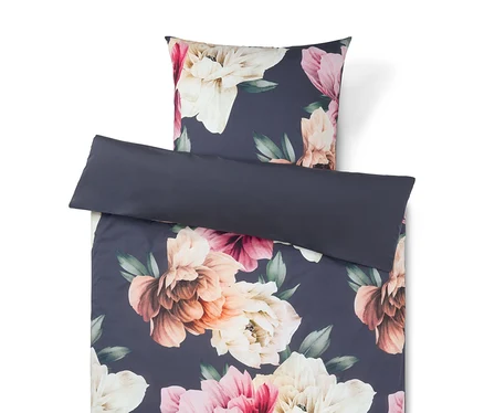 Parure de lit florale sur fond bleu foncé avec de grandes fleurs roses, crème et pêche. Un oreiller uni bleu foncé est posé dessus.