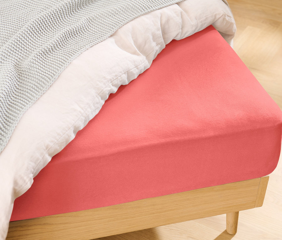 Gros plan d'un lit avec un drap-housse en jersey orange de taille standard.