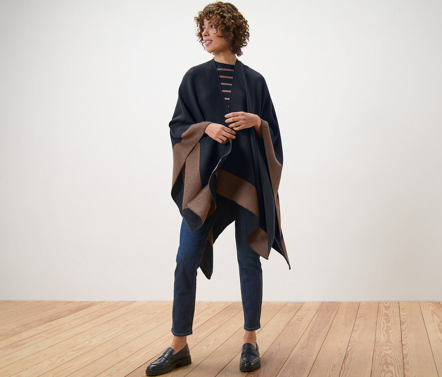 Une femme debout sur un plancher en bois porte un poncho tendance.