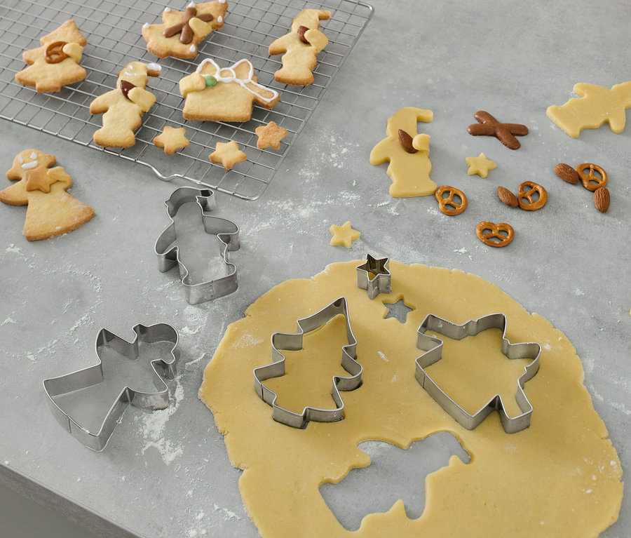 5 emporte-pièces pour biscuits sont posés sur un rouleau à pâtisserie et découpent des formes dans la pâte à biscuits.