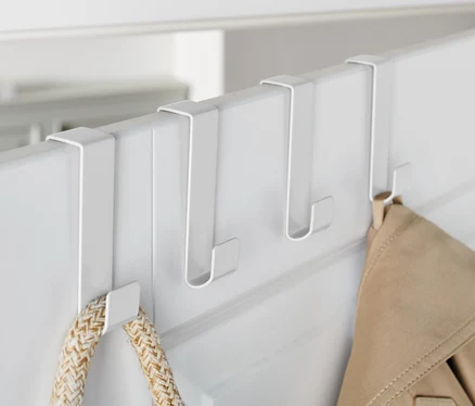 Trois crochets de porte blancs sont accrochés à une porte blanche, sur lesquels sont suspendus une veste et un sac.