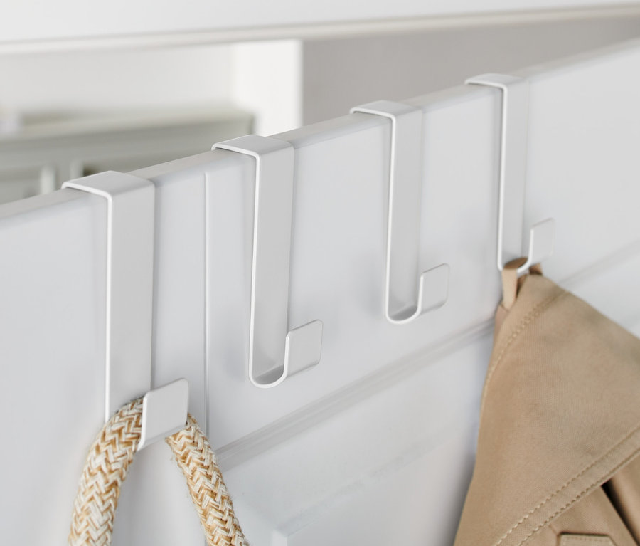 Trois crochets de porte blancs sont accrochés à une porte blanche, sur lesquels sont suspendus une veste et un sac.