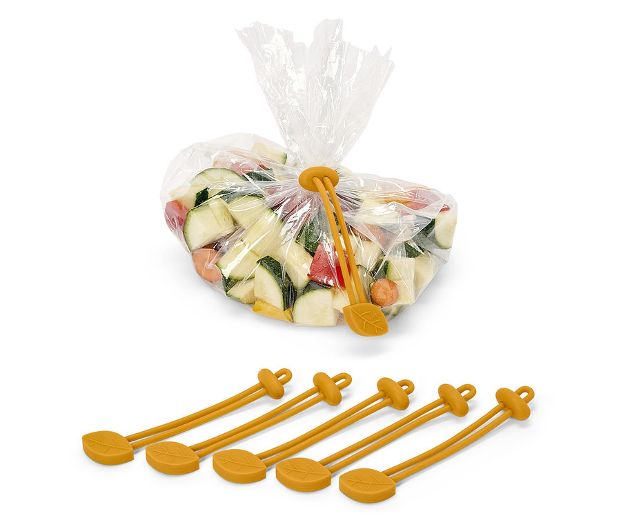 Des cubes de courgettes, de carottes et de poivrons dans un sac en plastique, fermé par une bande de serrage en silicone jaune à motif de feuille. Sous le sac, il y a quatre bandes de silicone jaunes.