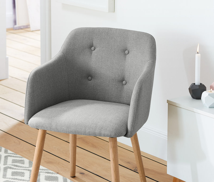 Une chaise rembourrée gris clair est posée sur un plancher en bois à côté d'une commode blanche.