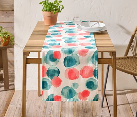 Une table en bois avec une nappe à cercles bleus et rouges, de la vaisselle et une plante en pot dessus.