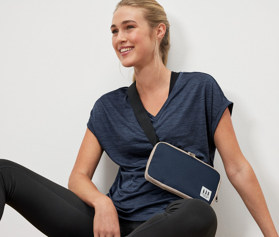 Une femme est assise par terre avec un sac multifonction en bandoulière.