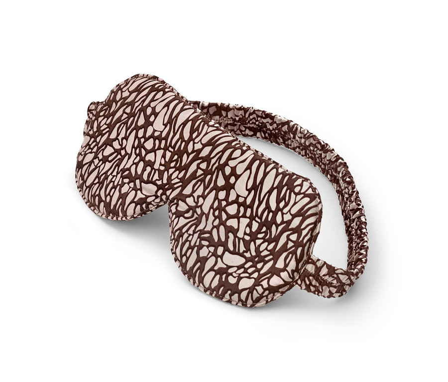 Un masque de nuit marron et crème posé sur un fond blanc.