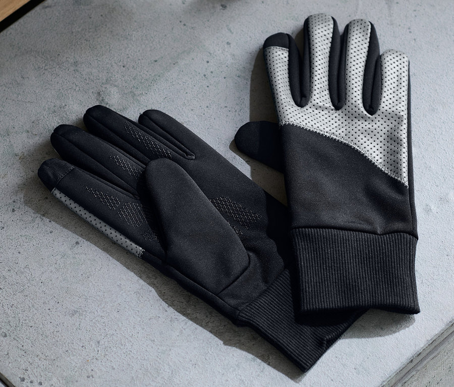 Deux paires de gants coupe-vent posées sur une surface grise à côté d'écouteurs et d'une bouteille d'eau.