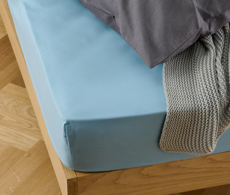 Un drap-housse en microfibres bleu clair sur un lit avec un oreiller gris et une couverture tricotée grise.
