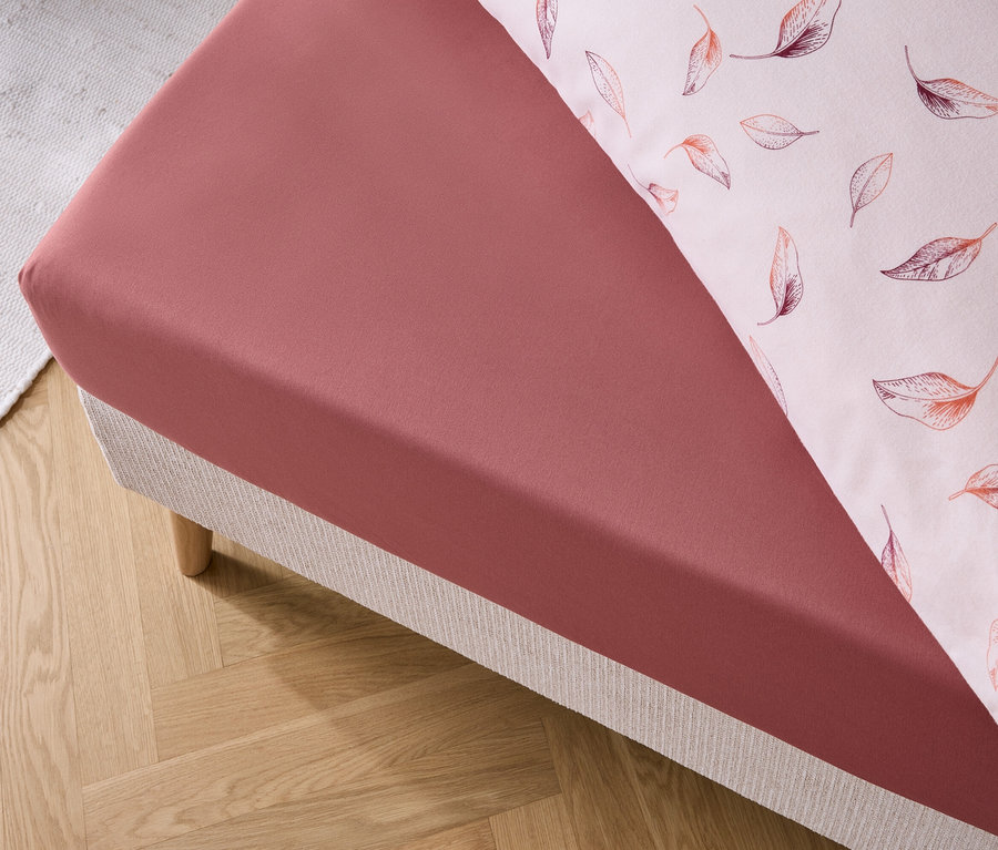 Détail d'un drap-housse rouge et d'une taie d'oreiller à motifs de feuilles sur un lit.