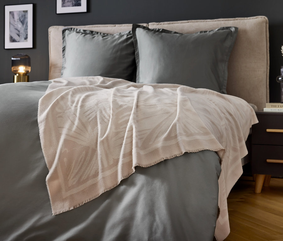 Chambre avec literie grise et couverture beige à imprimé feuilles.