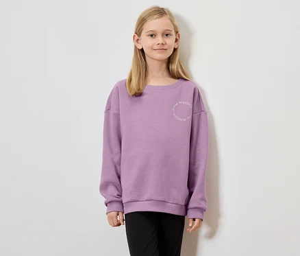 Fille aux cheveux blonds portant un sweat-shirt violet avec l'inscription "nonstop motion".