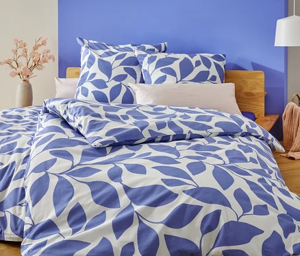 Un lit avec une literie à feuilles bleues et blanches se trouve devant un mur peint en bleu et blanc.