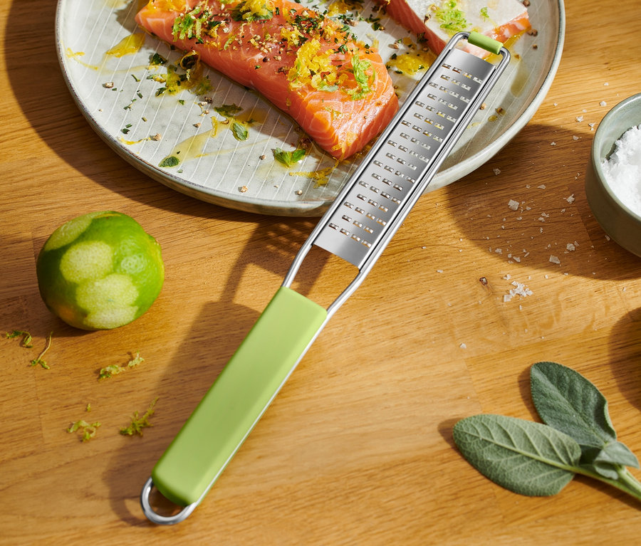 Un saumon sur une assiette, recouvert de zeste d'agrumes. A côté se trouve une râpe fine.