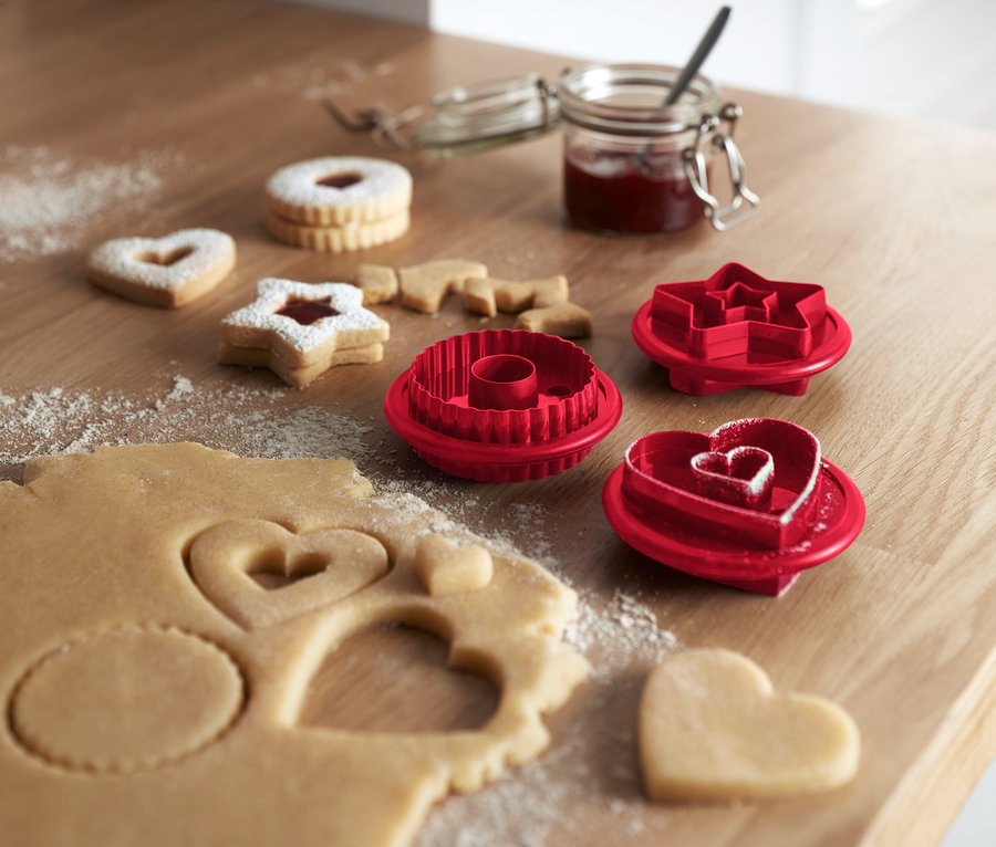 Sur une table en bois sont posés des sablés Linzer et 3 emporte-pièces pour sablés Linzer.