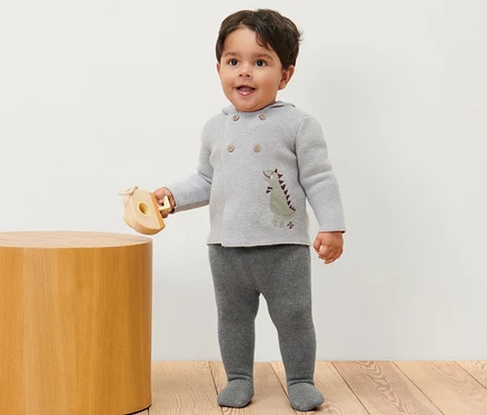 Un garçon est debout et tient un jouet en bois, il porte 2 collants thermiques pour bébé chinés.