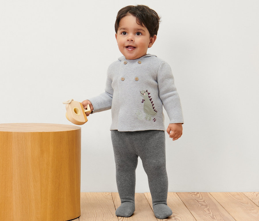 Un garçon est debout et tient un jouet en bois, il porte 2 collants thermiques pour bébé chinés.