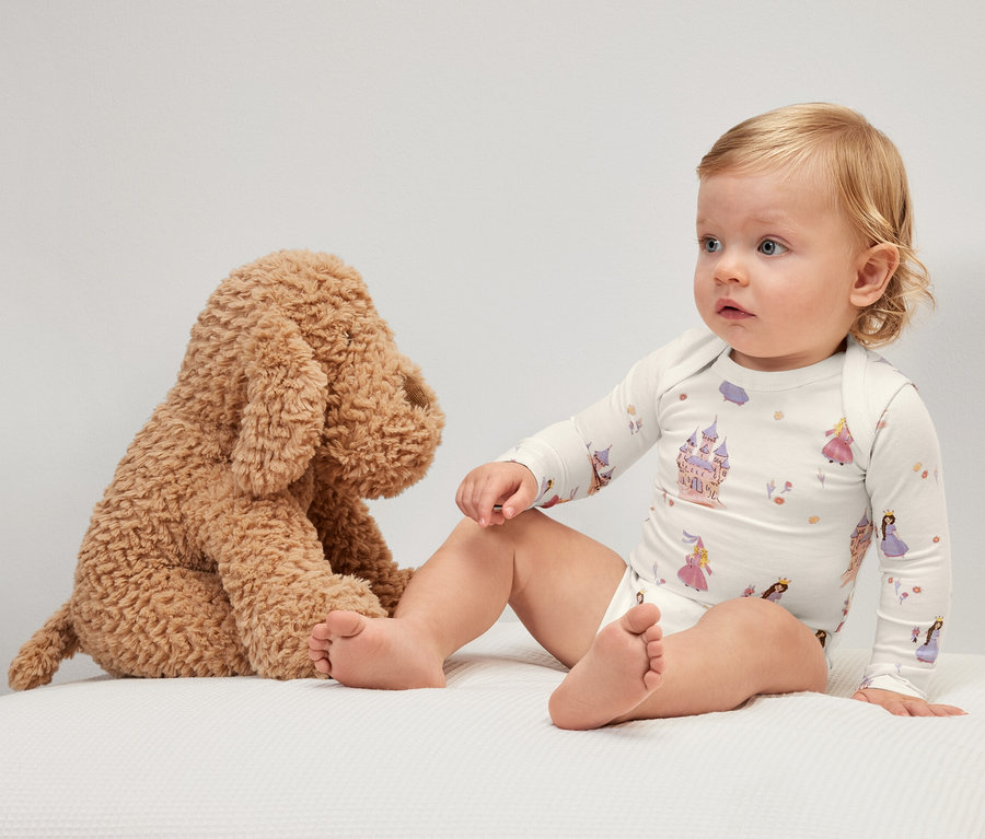 Bébé est assis à côté d'un chien en peluche et porte un body évolutif avec un motif de princesse.