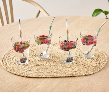 Quatre verres avec de l'eau, des fruits et 4 cuillères sur une table.