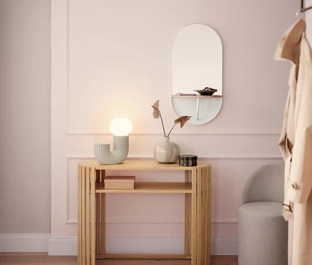 Un couloir lumineux avec une console en bois, une lampe, un miroir et un tabouret gris.