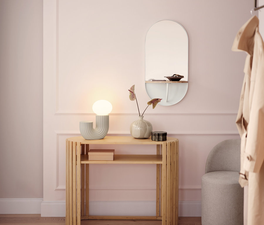 Un couloir lumineux avec une console en bois, une lampe, un miroir et un tabouret gris.