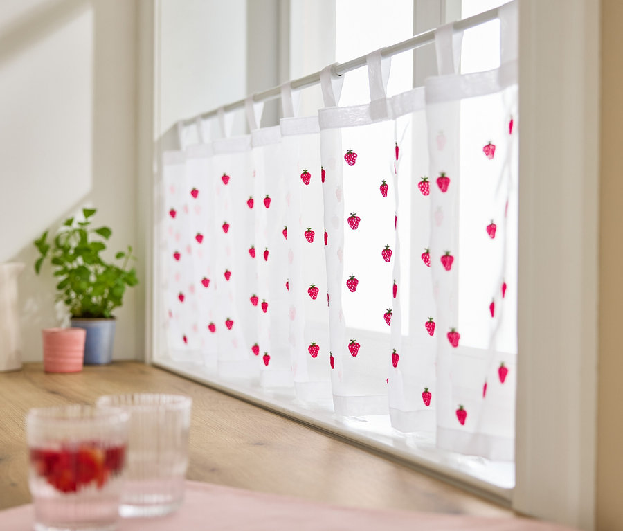 Des rideaux bistrot brodés avec des motifs de fraises sont accrochés à la fenêtre.
