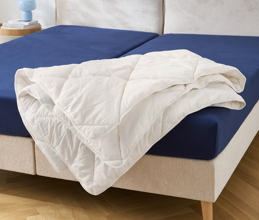 Sur un lit avec un drap-housse bleu se trouve une couette blanche.