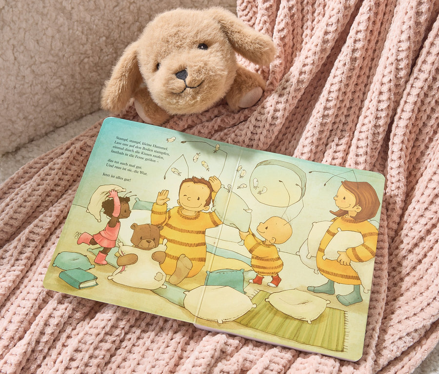 Un chien en peluche est posé sur le livre « Bébé Bourdon Bommel » (en allemand) et une couverture tricotée rose.