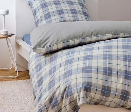 Lit avec des draps à carreaux bleu et blanc et un oreiller gris.