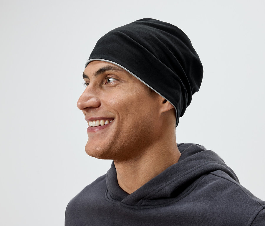 Profil d'un homme souriant portant un bonnet noir et un sweat à capuche gris.