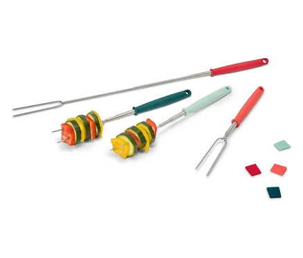 Quatre brochettes de barbecue, dont deux avec des légumes, sont posées sur un fond blanc. Les brochettes ont des manches rouges, verts et orange.