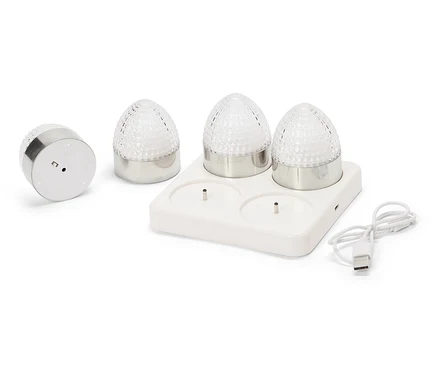 Quatre petites lampes rondes avec des bases argentées et des coupoles en verre transparent à facettes sont posées sur une station de charge blanche avec un câble USB.