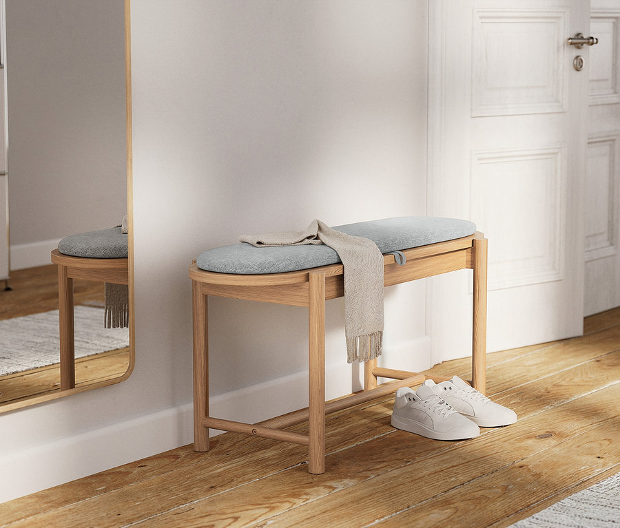 Un banc en bois clair avec un coussin bleu clair et un foulard beige posé dessus. Des baskets blanches sont posées en dessous.