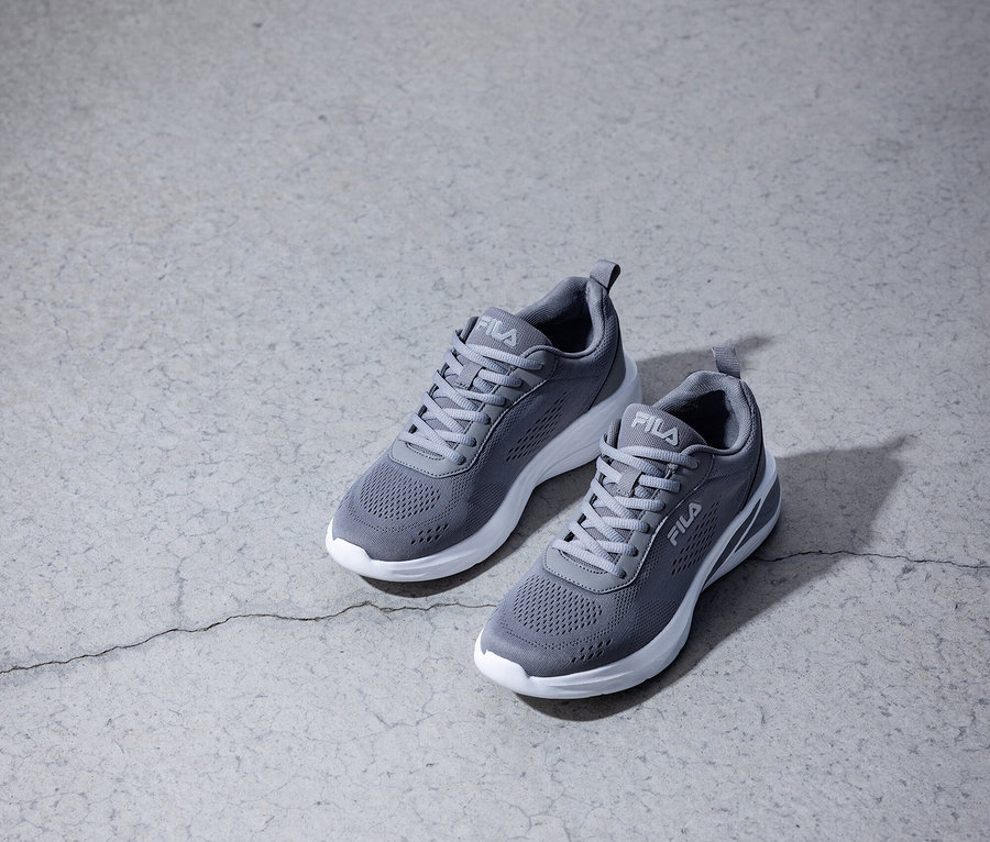 Deux baskets Fila grises avec des semelles blanches sur un sol en béton gris.