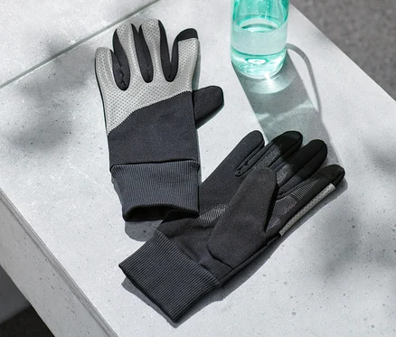 Deux gants coupe-vent avec parementure réfléchissante reposent sur une surface grise à côté d'une bouteille d'eau.