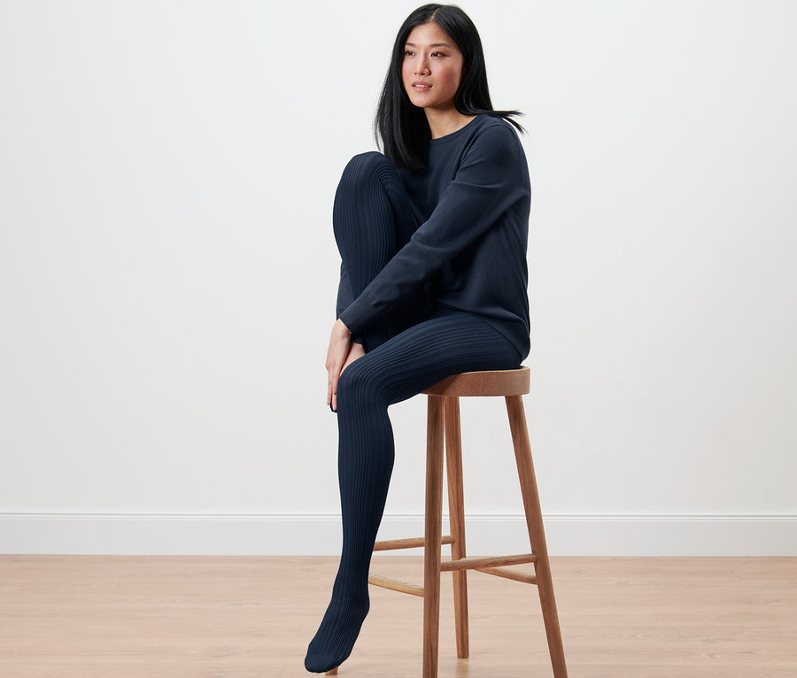 Une femme est assise sur un tabouret et porte des collants fins à motifs.