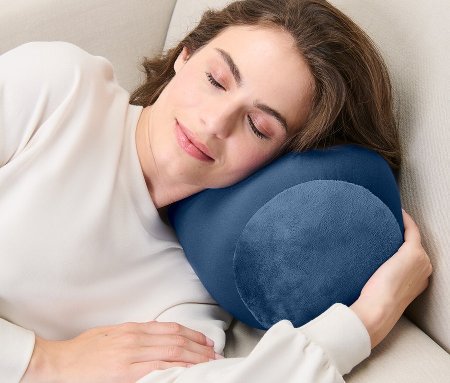 Une femme dort sur un canapé beige avec un coussin de relaxation.
