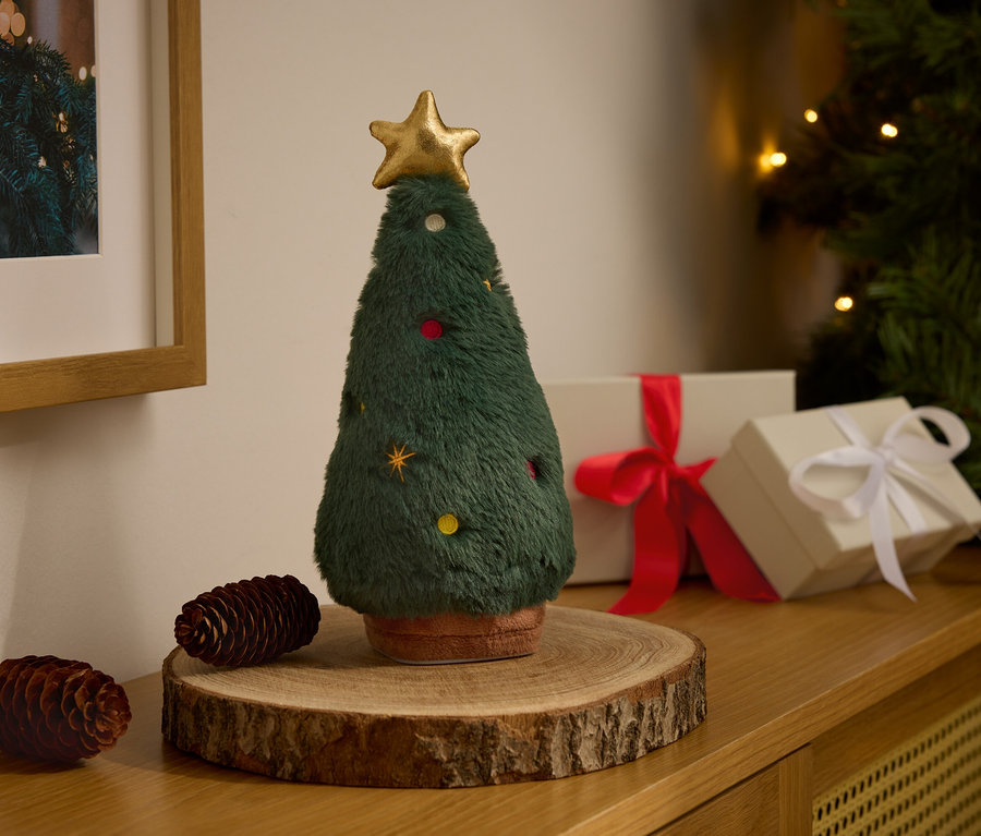 Un arbre de Noël décoratif en peluche avec une étoile dorée est posé sur un socle en bois à côté de deux pommes de pin et de boîtes cadeaux.
