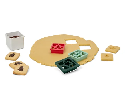 Pâte avec des emporte-pièces en forme d'arbre, d'étoile et d'ornement, des biscuits finis et un récipient blanc avec du glaçage.