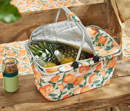 Panier isotherme avec des fruits et des boissons sur une table en bois.