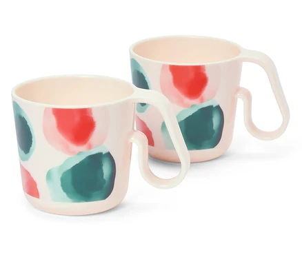Deux tasses roses à motifs de points rouges et verts sont posées sur un fond blanc.