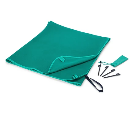 Une serviette turquoise est partiellement pliée à côté d'un petit sac et de piquets sur un fond blanc.