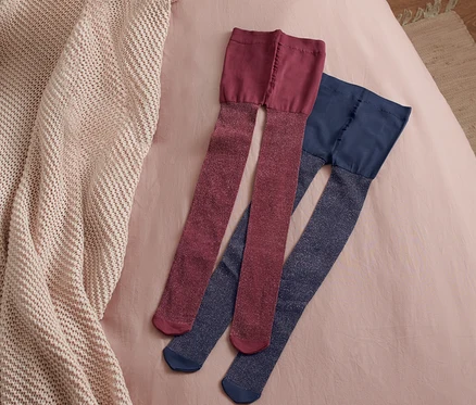 Deux paires de collants enfant sont posées sur un drap rose à côté d'une couverture en tricot beige.