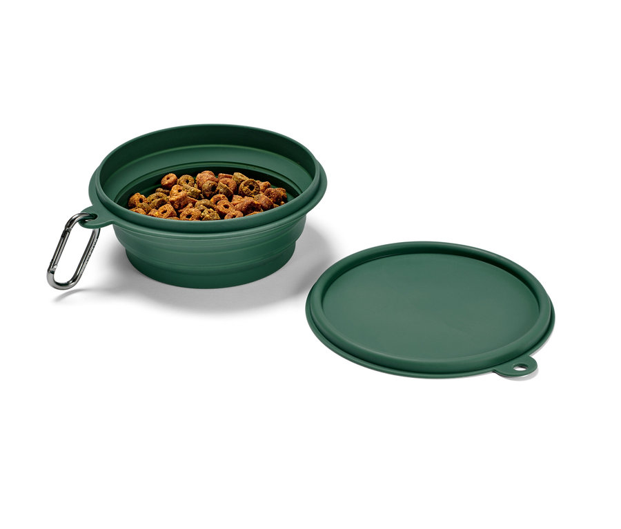 Un gamelle repliable verte remplie de nourriture sèche pour animaux, avec un mousqueton et un couvercle à côté.