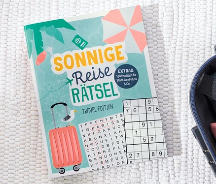 Le livre « Sonnige Reise Rätsel » est posé à côté d'une valise ouverte.