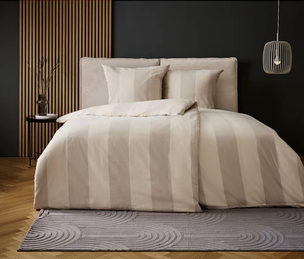 Chambre avec literie à rayures beiges et tapis gris à motif circulaire.